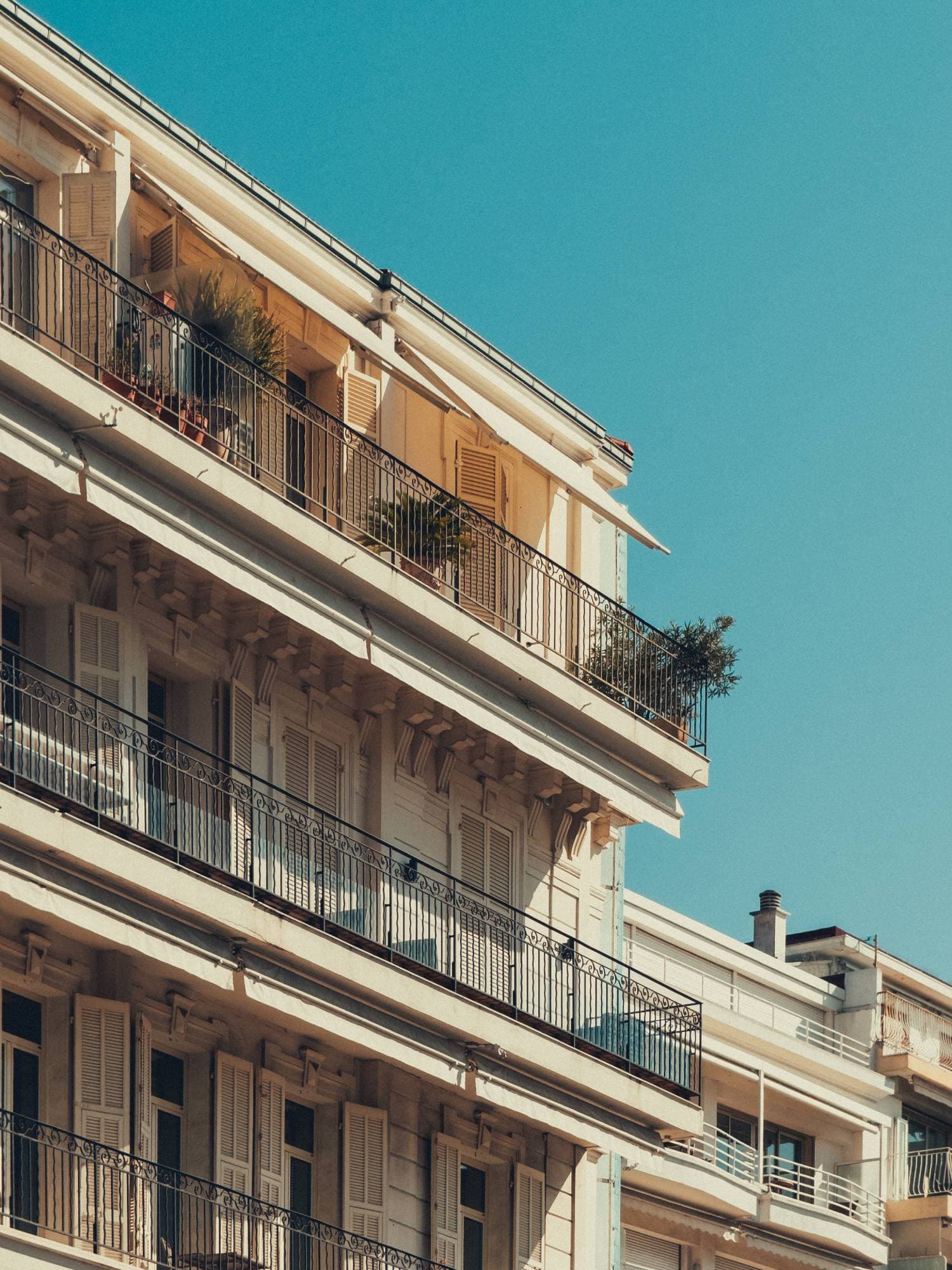 Cream apartment building with wrought-iron balconies against a clear sky, edited